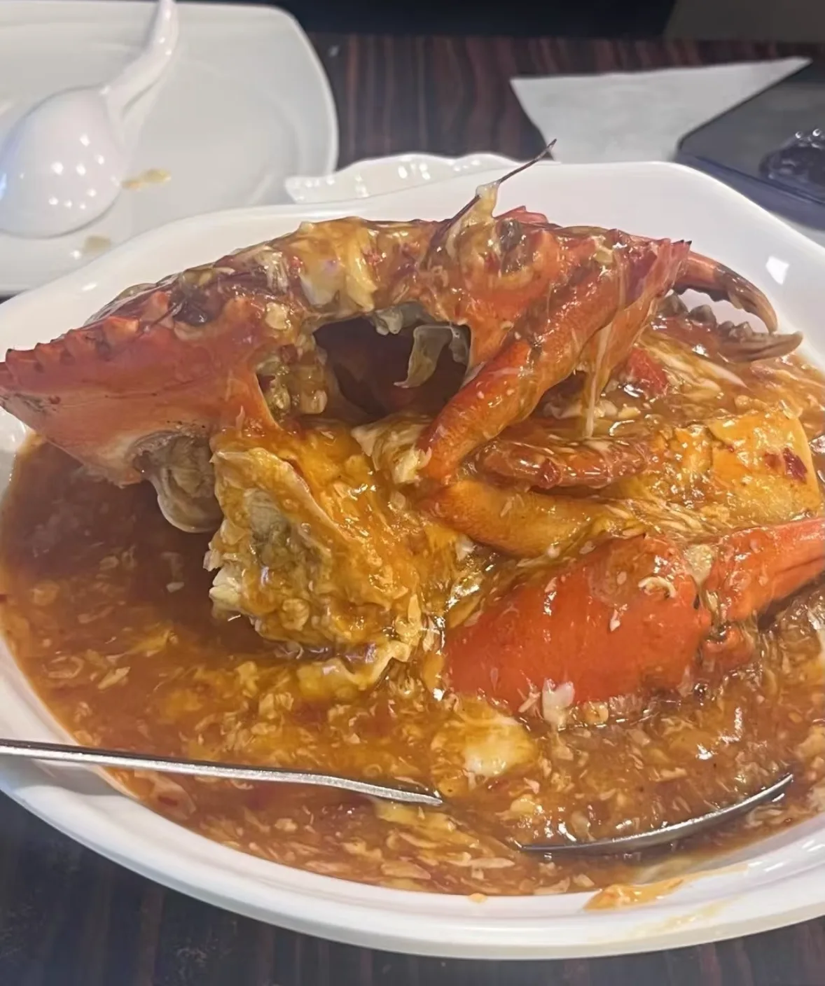 A plate of Singapore chili crab in thick red sauce with a spoon resting in the dish